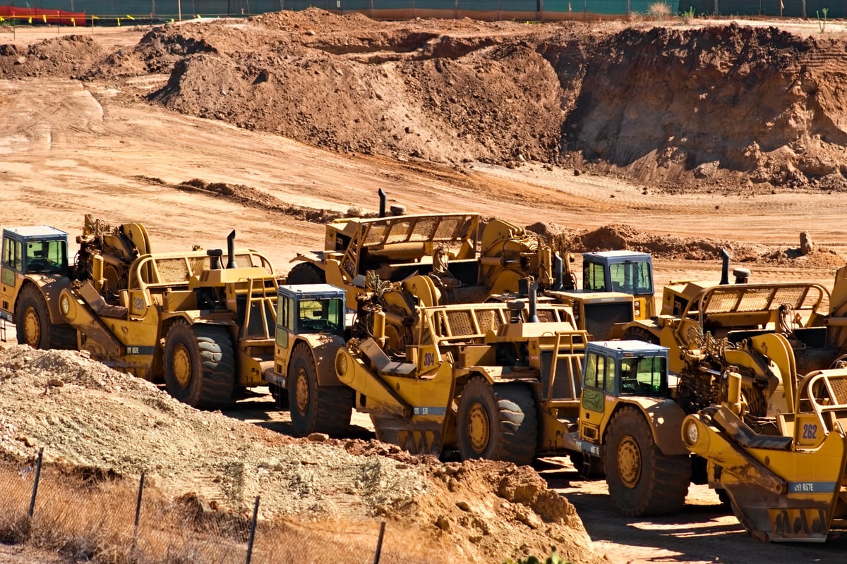 Rows of yellow earthmoving machinery on a dusty construction site under bright sun