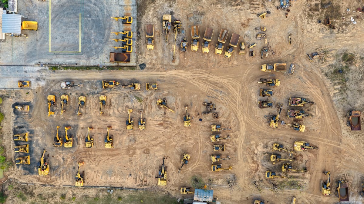 Yellow excavators and dump trucks parked in rows on a dirt yard awaiting sale